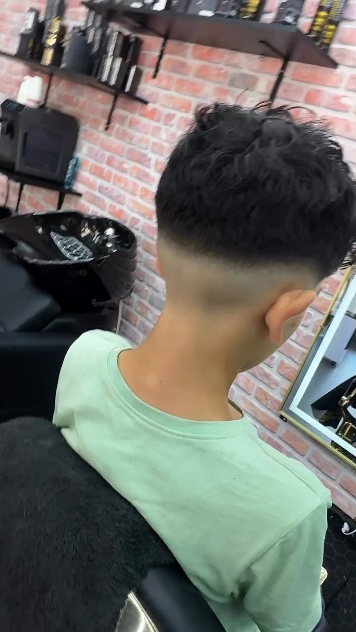 Skin fade bij een jonge klant, van achteren gezien voor de bakstenen muur