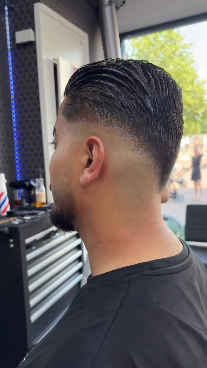 Zijaanzicht van een slick back met fade, raam met bomen op de achtergrond